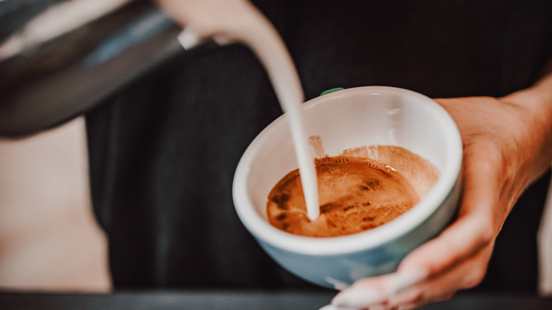 A person pouring creamer into a cup of coffee