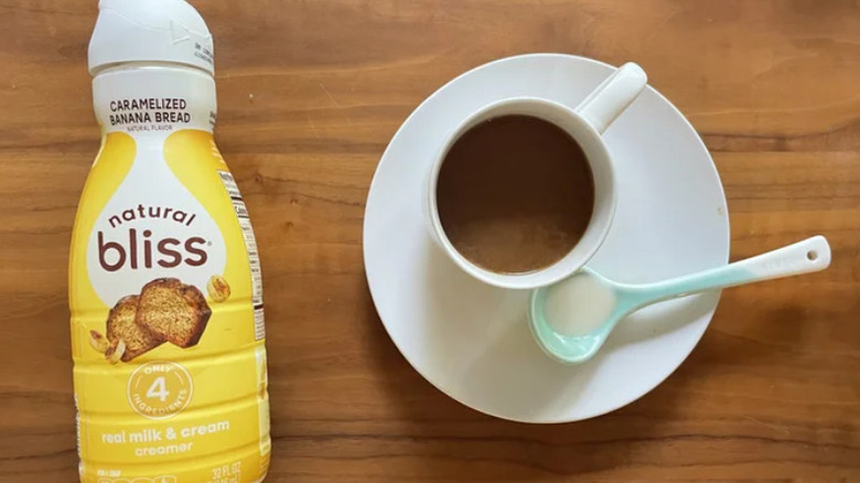 A bottle of Natural Bliss creamer sits near a cup of coffee in a saucer