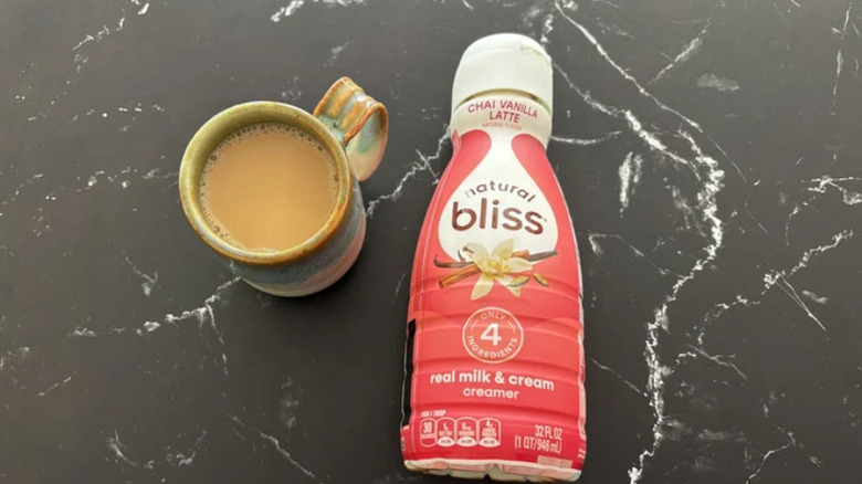 A cup of coffee and a bottle of coffee creamer on a marble surface