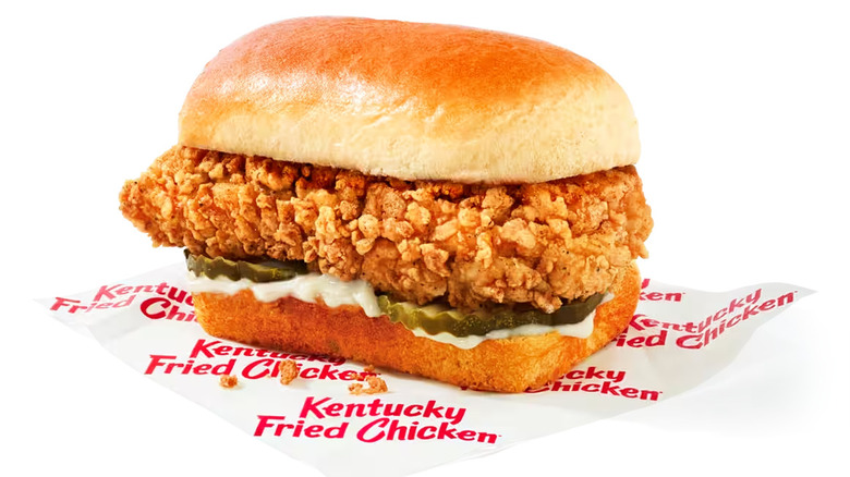 KFC Snacker fried chicken sandwich sitting on wax paper with logo against white backdrop