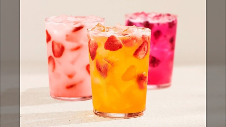 Pink, dark pink, and orange Starbucks Refresher drinks in glasses with strawberry pieces inside