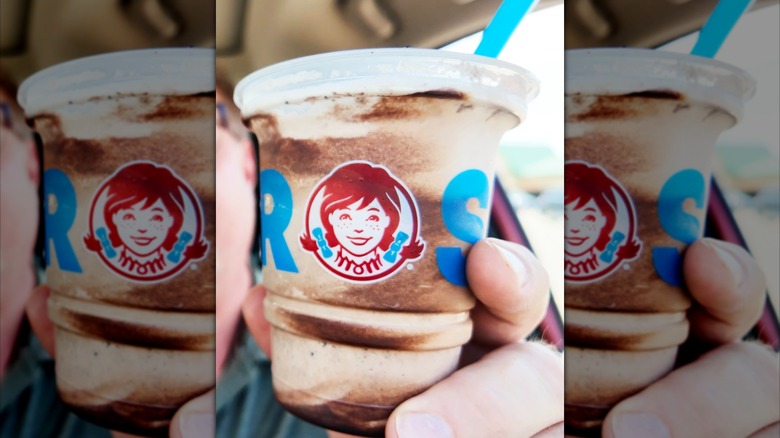 Hand holding plastic cup of Wendy's Cookie Dough Frosty Fusion dessert with blue straw