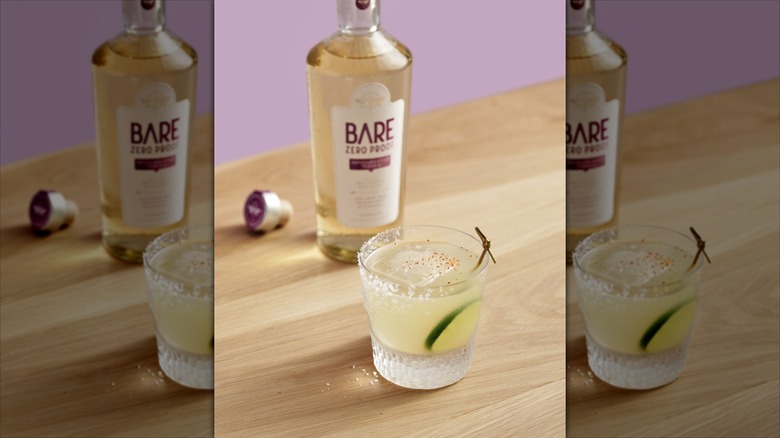 Bottle of Bare zero proof behind glass with cocktail on wooden table