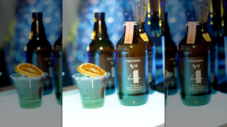 Curious No. 4 Elixir next to cup with drink and orange slice on white table