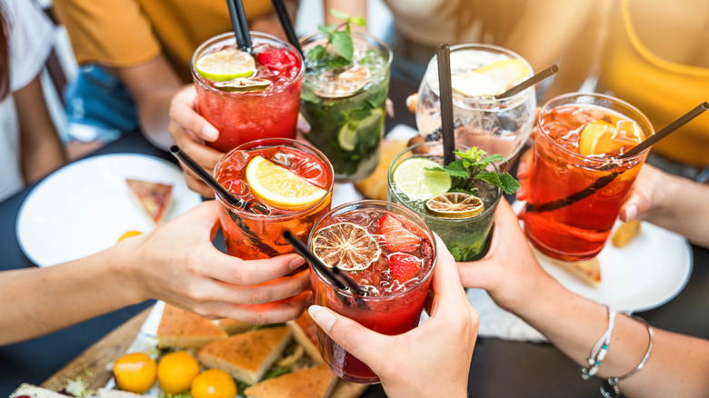 Hands holding cocktails clinking glasses together over table