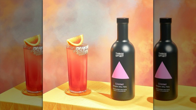 Bottle of Three Spirit Livener next to highball glass on wooden surface