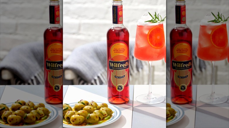 Bottle of Wilfred's aperitif next to glass with cocktail and plate of olives