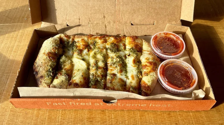Cheese and pesto garlic bread in cardboard takeout box with two tubs of marinara sauce