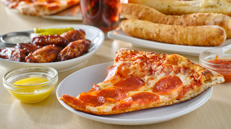 Slice of pizza on plate with chicken wings and breadsticks in background