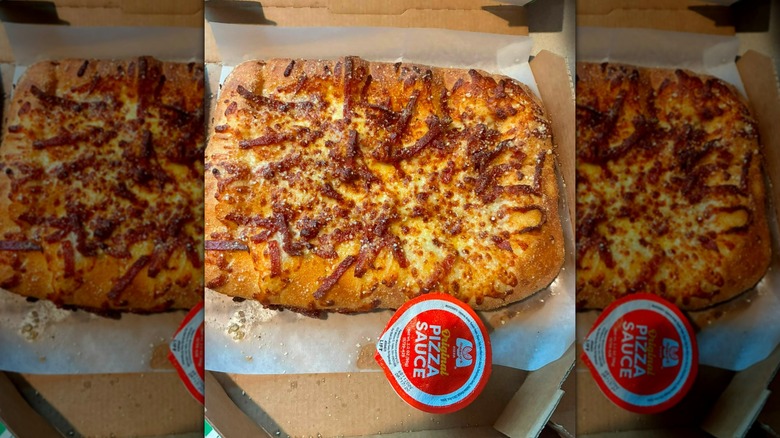 Pepperoni pizza bread in cardboard takeout box with tub of pizza sauce