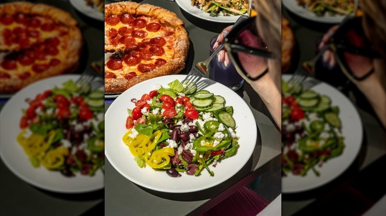 Plate of Greek salad next to pepperoni pizza