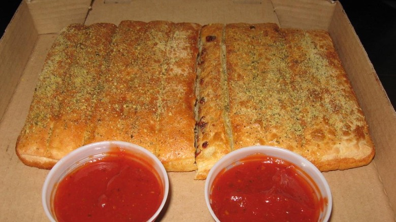 Pizza Hut breadsticks in cardboard takeout box with two pots of marinara sauce