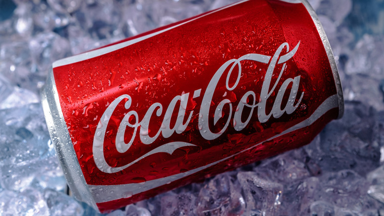 Can of Coca-Cola on a bed of ice over a blue background.
