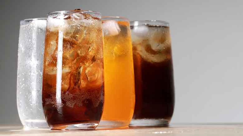Tumblers full of ice and soft drinks of various colors against white background.
