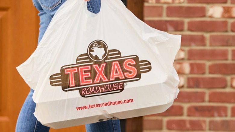 person carrying a takeout bag of Texas Roadhouse food