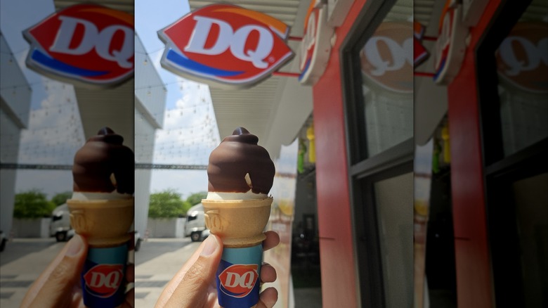 hand holding a chocolate-dipped soft serve ice cream cone in front of a Dairy Queen, mirrored