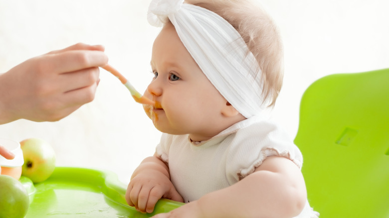 A mother feeds a baby with a spoon of fruit puree