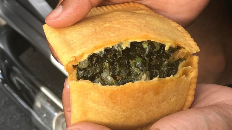 Hands holding a spinach Jamaican Pattie from Simply Wholesome