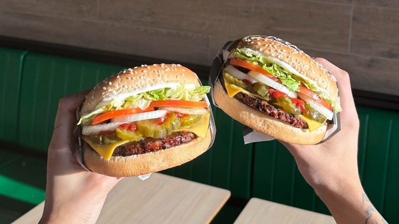 Hands holding two Burger King vegetarian burgers with tomatoes, onions, lettuce, and pickles