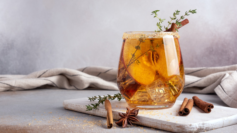 Homemade ice sweet apple cider, cocktail or mocktail with cinnamon, thyme and anise in glass for tasty and refreshing break on grey kitchen background