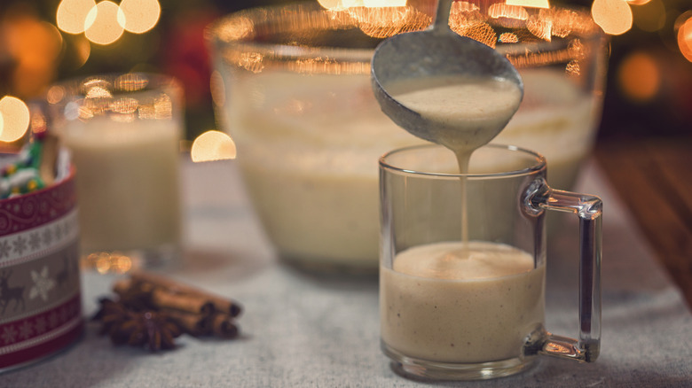 Young women pouring fresh homemade eggnog with cinnamon at Christmas time