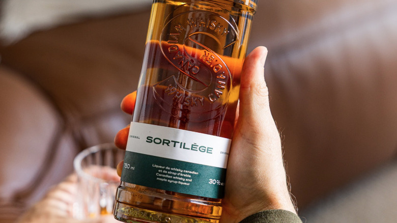 Man's hands holding glass bottle of Sortilège
