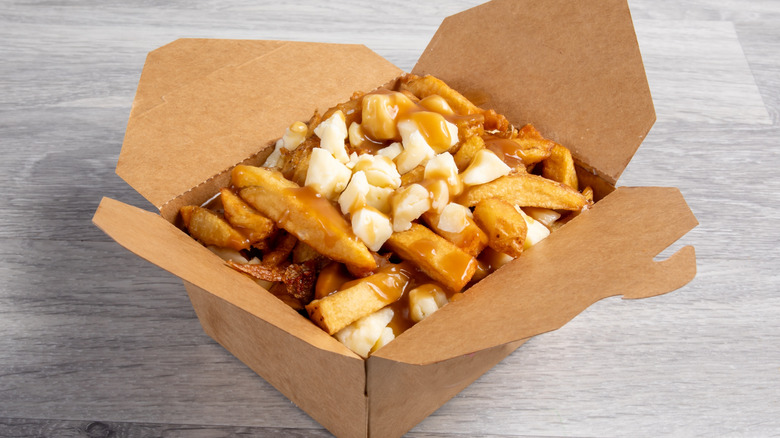 Cardboard takeout container of poutine french fries with cheese curds and gravy