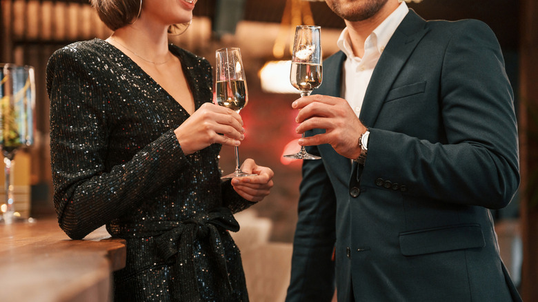 Elegantly dressed couple holding champagne glasses in a formal restaurant setting