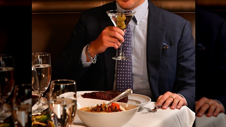 A man in a suit holding a martini and dining at Mastro's restaurant