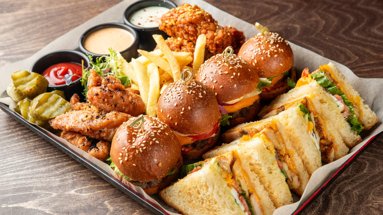Large food platter featuring club sandwiches, burgers, wings, sauces, and pickles