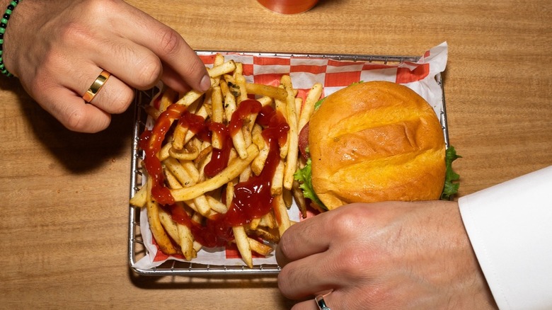 Hands reaching for Smashburger burger and fries