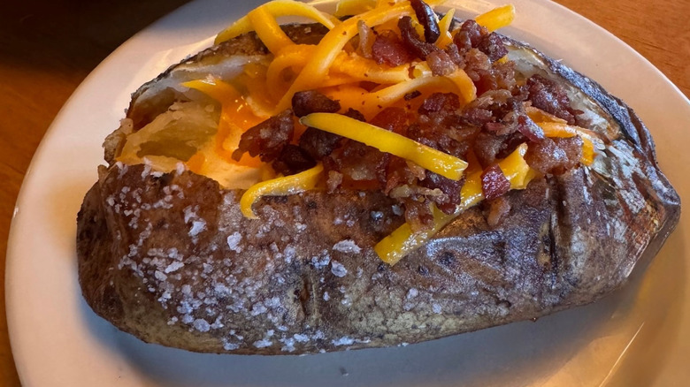 Baked potato on plate with butter, shredded cheddar cheese, bacon and salt