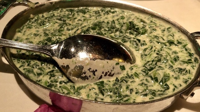 Spoon in the middle of a dish containing creamy chopped spinach