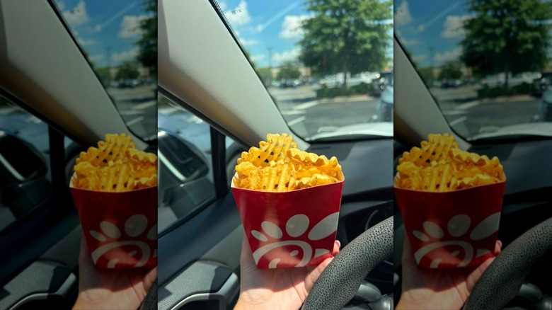 Hand holding carton of Chick-fil-A fries in car
