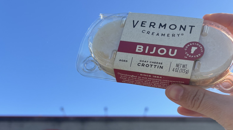 Hand holding package of Vermont Creamery Bijou Goat Cheese against blue sky