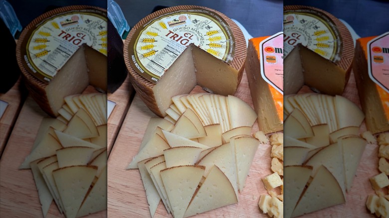 Cut wheel of El Trigal 6 Months Aged Manchego on wooden cutting board