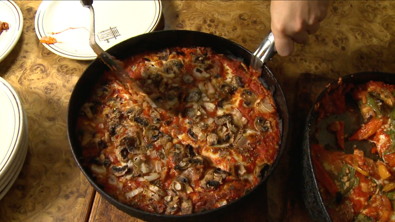 A deep dish pizza being sliced in a pan