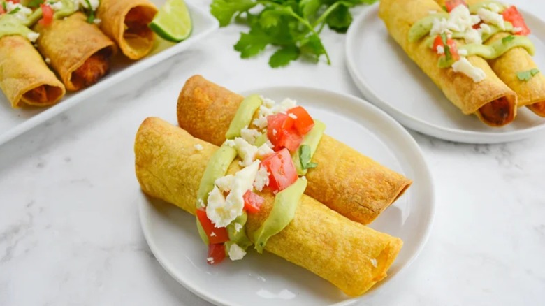 Air fryer taquitos with avocado crema on white plate