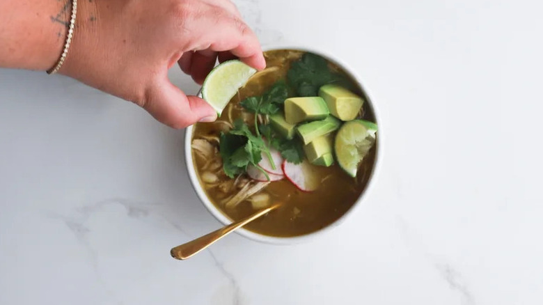 Hand squeezing lime into Slow Cooker Chicken Posole Verde