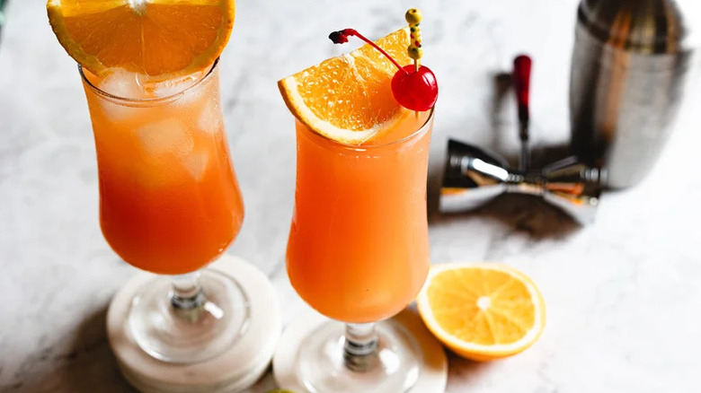 Two Hurricane cocktails with garnishes alongside shaker tin and jigger.