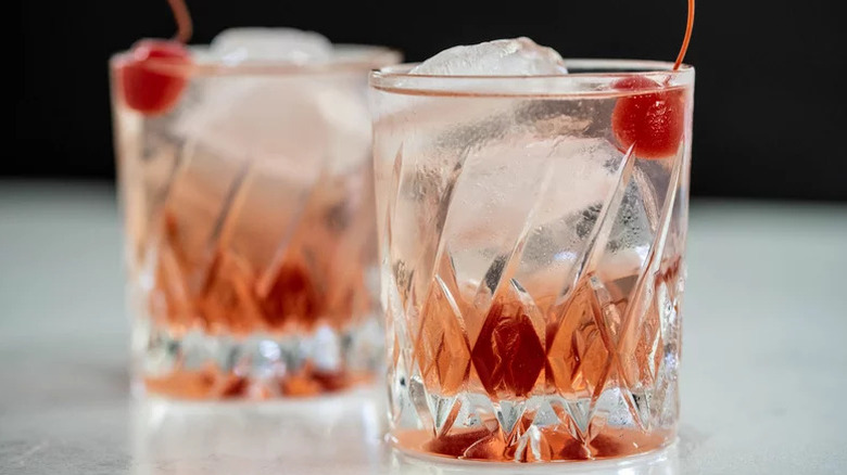 Two crystal rocks glasses with a cherry ombre over large cubes and cherry garnish.