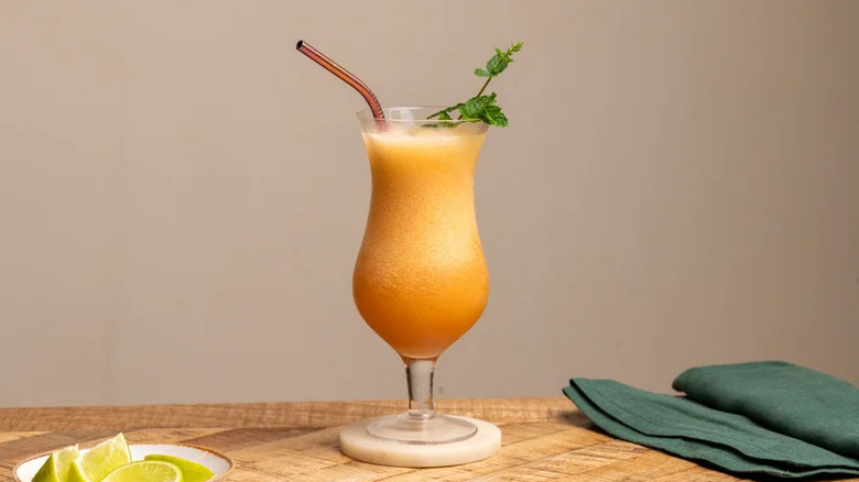 A frozen tropical drink in a Hurricane glass with mint sprig against plain background.