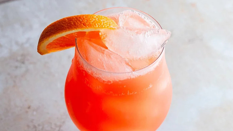 Aerial view of ruby red cockail in snifter glass with ice and orange wedge.