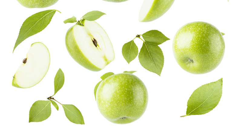 granny smith apples and green leaves against a white backdrop