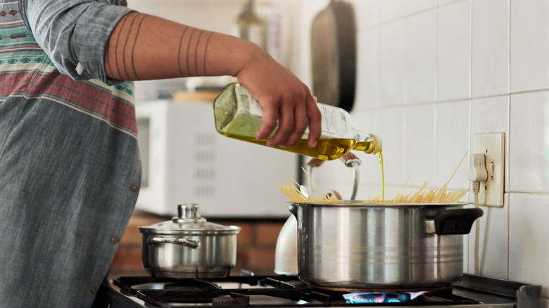 Person pouring oil into pot with spaghetti