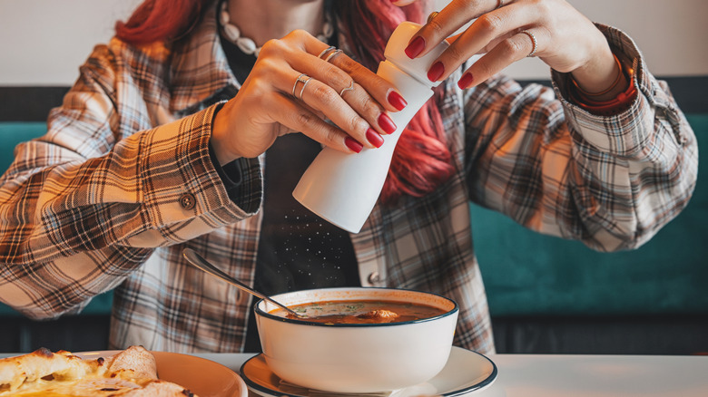 Woman adding salt to bowl of soup