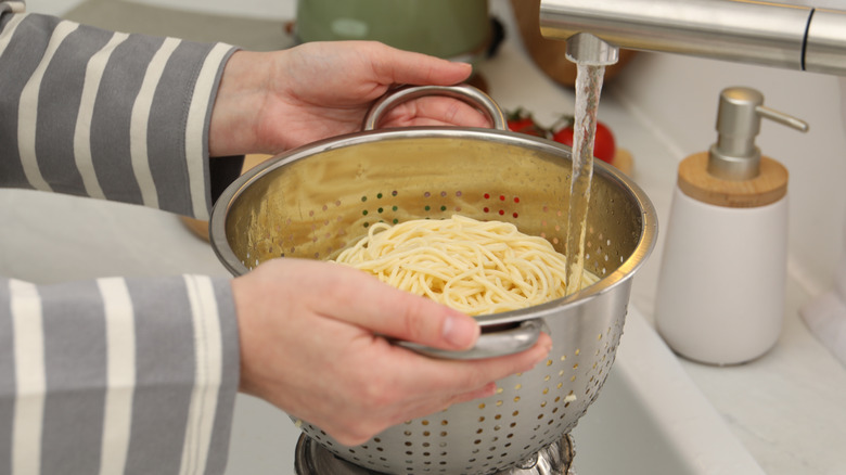 Person rinsing cooked pasta in colander