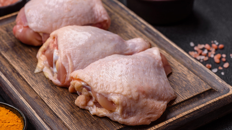 Raw bone-in chicken thighs on wooden board