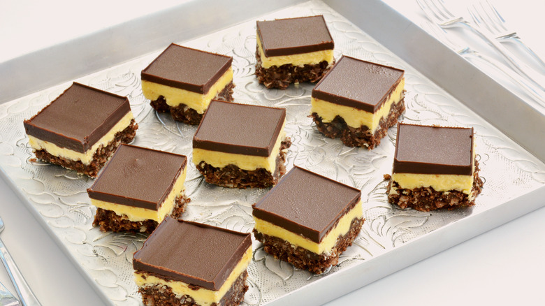 Fresh baked Nanaimo bars on vintage embossed metal tray and tiny forks in horizontal format.