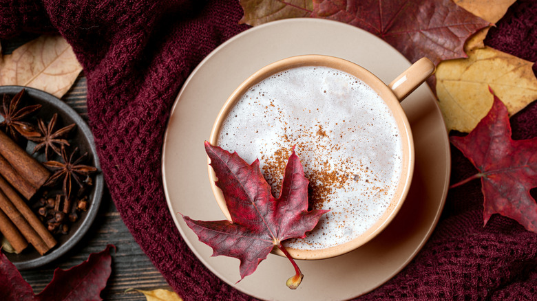 Maple latte in brown mug with maple leaves on a knitted cloth